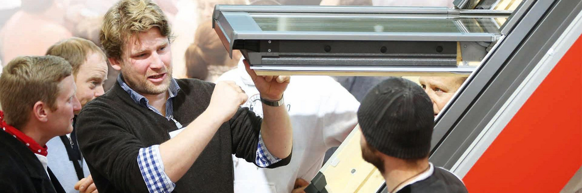Ein Mitarbeiter erklärt Handwerkern auf einer Messe ein Dachfenster 